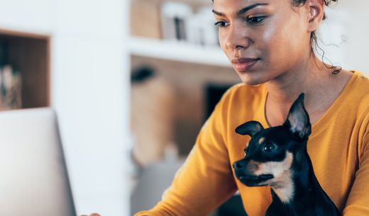 African American woman sitting with dog on her lap while working on the computer.
