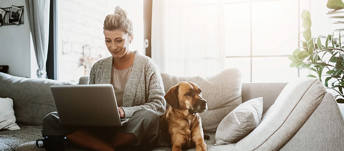 Woman working on laptop sitting next to dog.