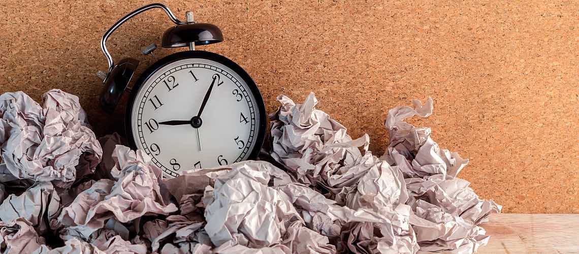 A small clock with crumpled papers around it.