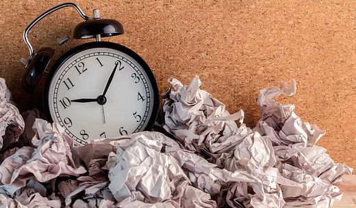 A small clock with crumpled papers around it.