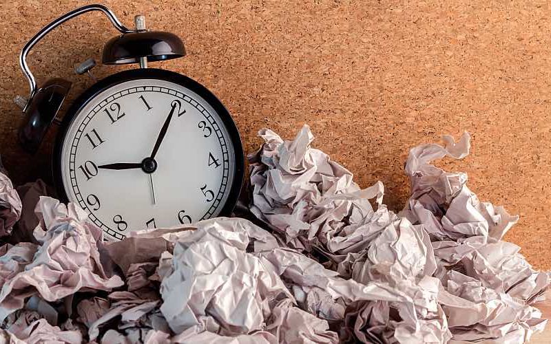 A small clock with crumpled papers around it.