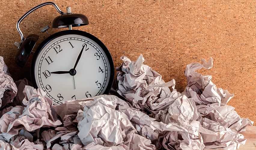 A small clock with crumpled papers around it.