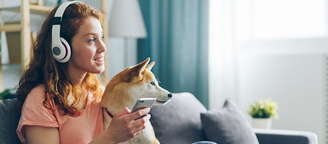 Woman listening to headphones while sitting on couch with her dog.