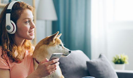 Woman listening to headphones while sitting on couch with her dog.