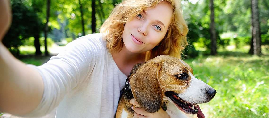 Young millennial taking selfie with dog in the park.
