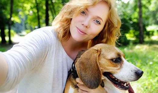 Young millennial taking selfie with dog in the park.