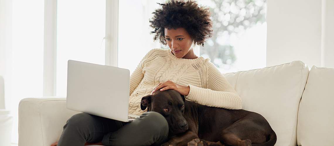 Woman uses computer while snuggling her dog on couch.