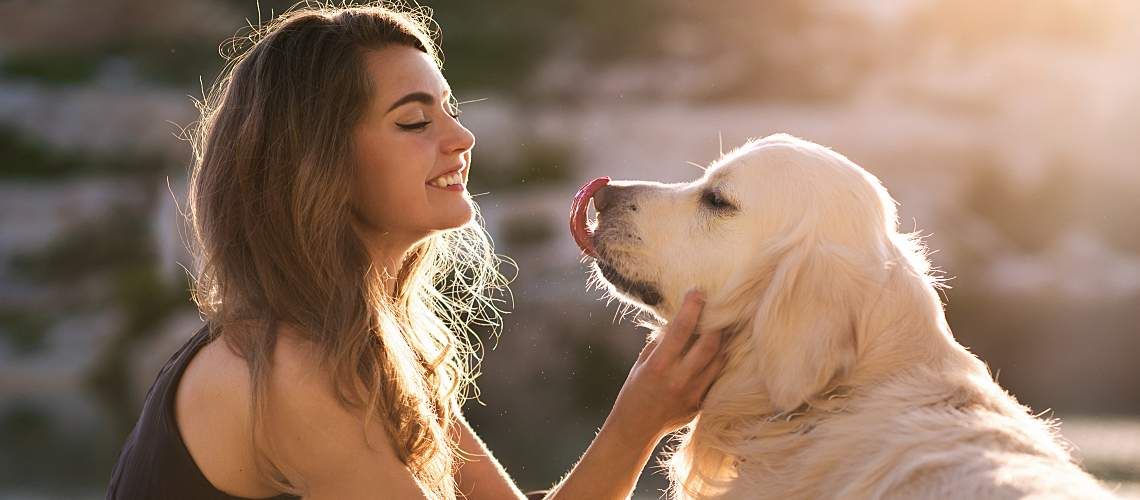 A young woman greets her dog outside.