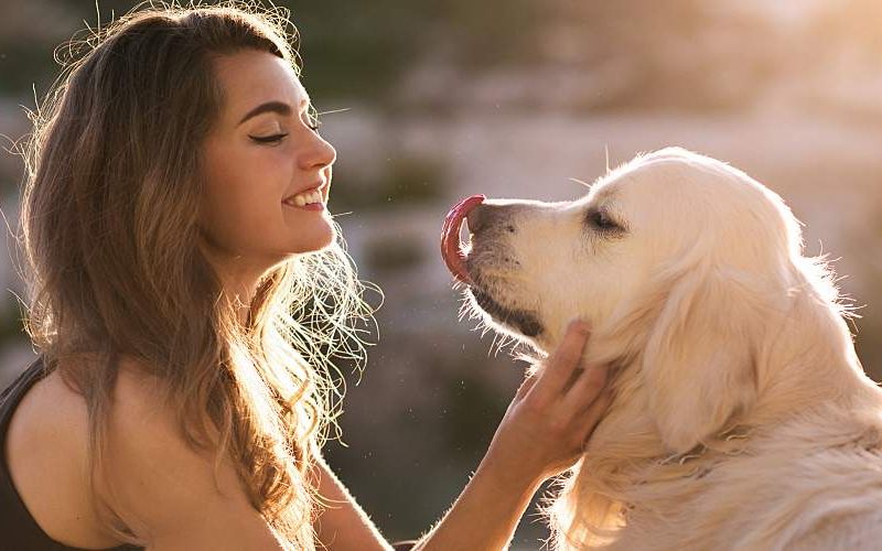 A young woman greets her dog outside.