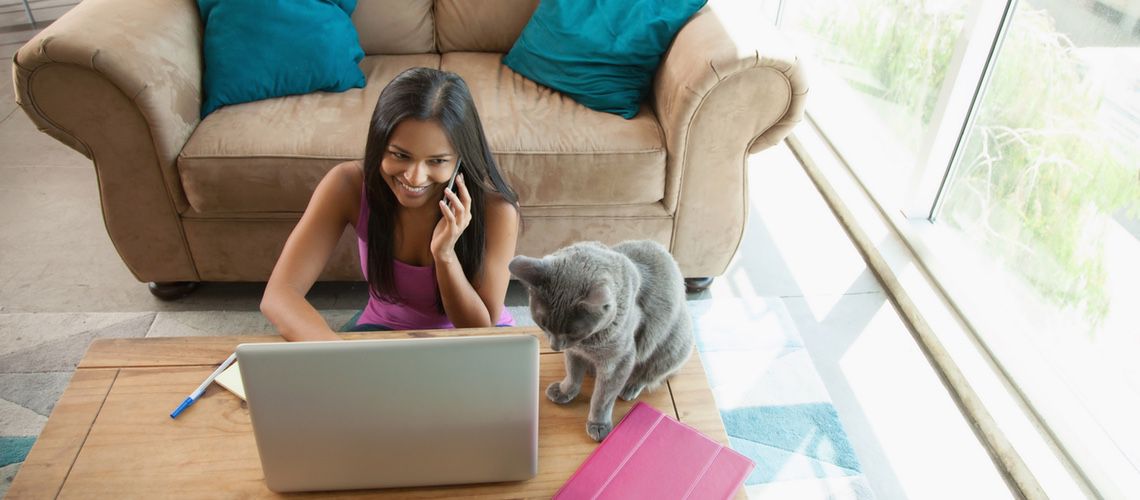 Woman on the phone sitting at her laptop with her cat.