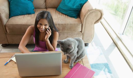 Woman on the phone sitting at her laptop with her cat.