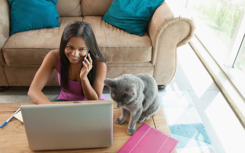 Woman on the phone sitting at her laptop with her cat.