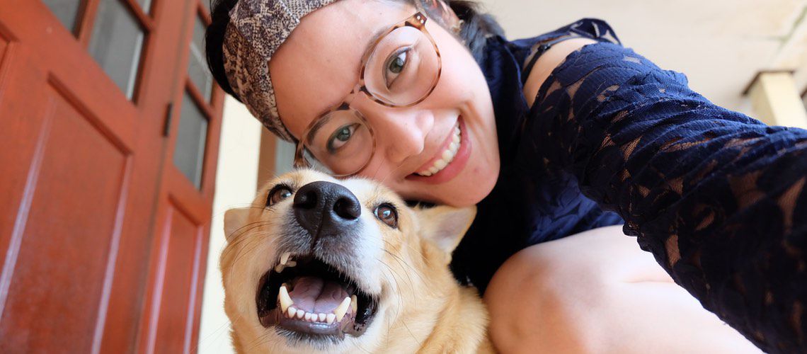 Asian woman taking a selfie with her dog while on the front step.