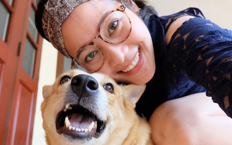 Asian woman taking a selfie with her dog while on the front step.