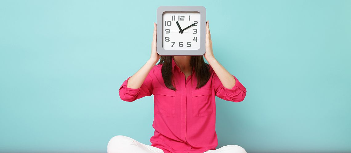 Woman holding a clock in front of her face.