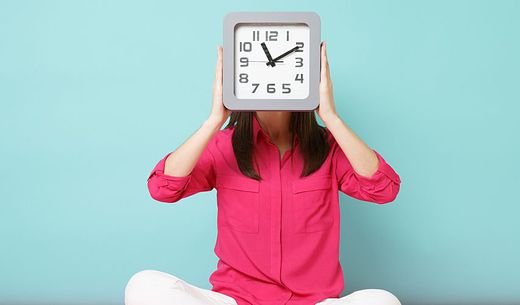 Woman holding a clock in front of her face.