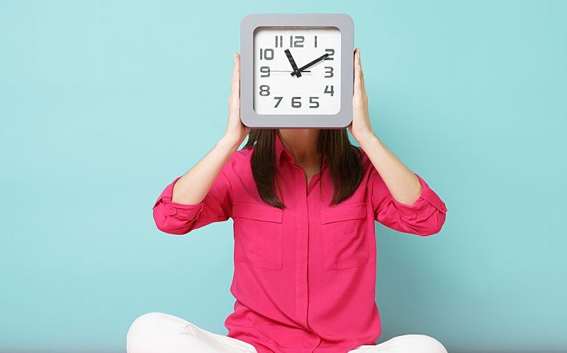 Woman holding a clock in front of her face.