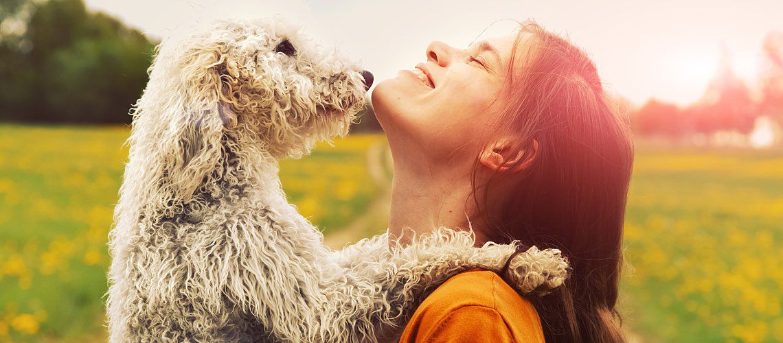 A woman and her pet dog embrace in a green field