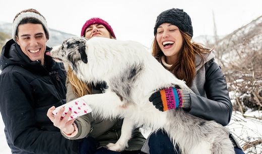 Group of young adults playing with a dog in the snow while taking a selfie.