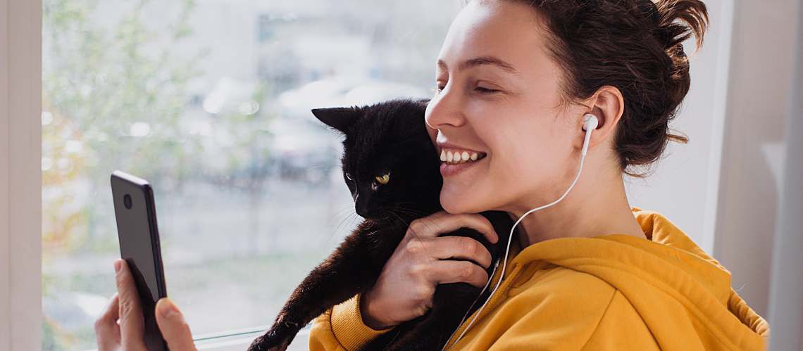 Young woman holding her cat and looking at her phone.