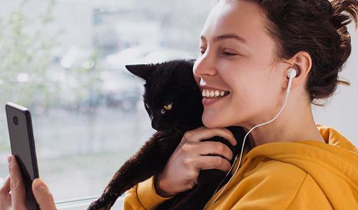 Young woman holding her cat and looking at her phone.