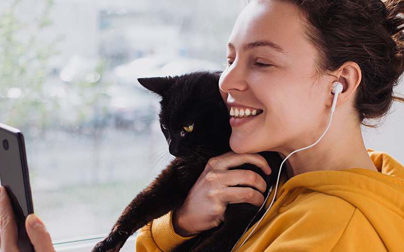 Young woman holding her cat and looking at her phone.