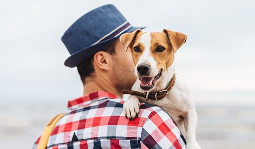 Young millennial hold his dog on a beach.