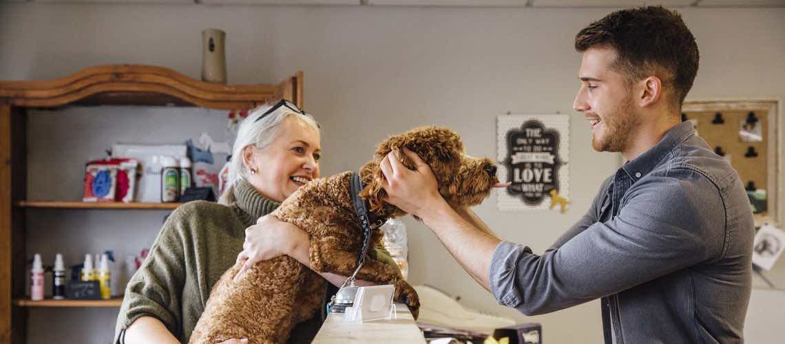 Veterinary receptionist greeting a female client and her dog.