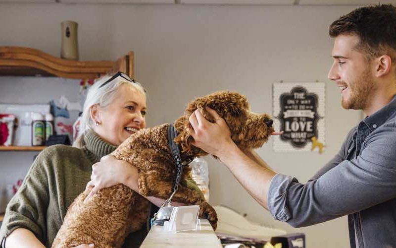 Veterinary receptionist greeting a female client and her dog.