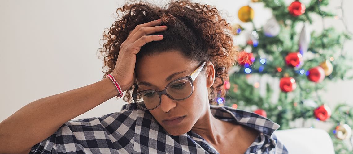 A young woman wearing glasses appears stressed in front of a Christmas tree