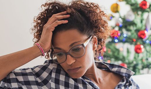 A young woman wearing glasses appears stressed in front of a Christmas tree