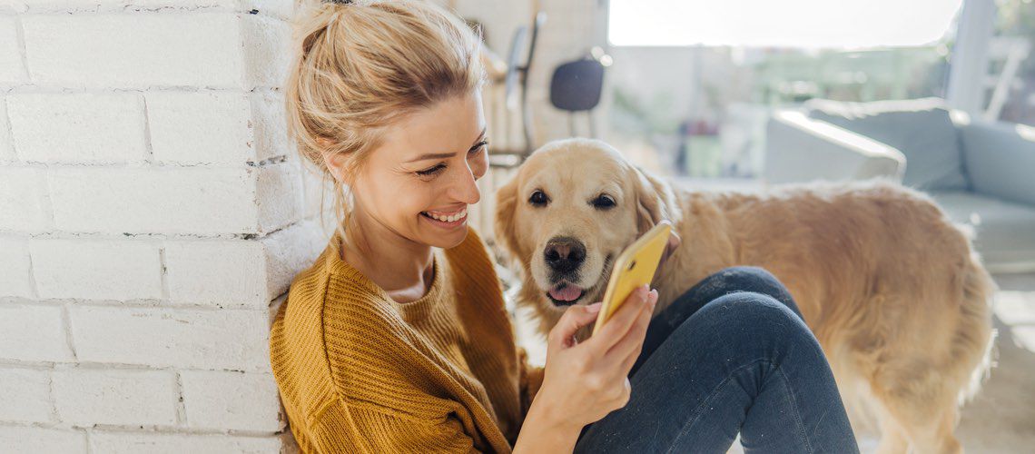 Millennial woman checking her phone with her dog next to her.