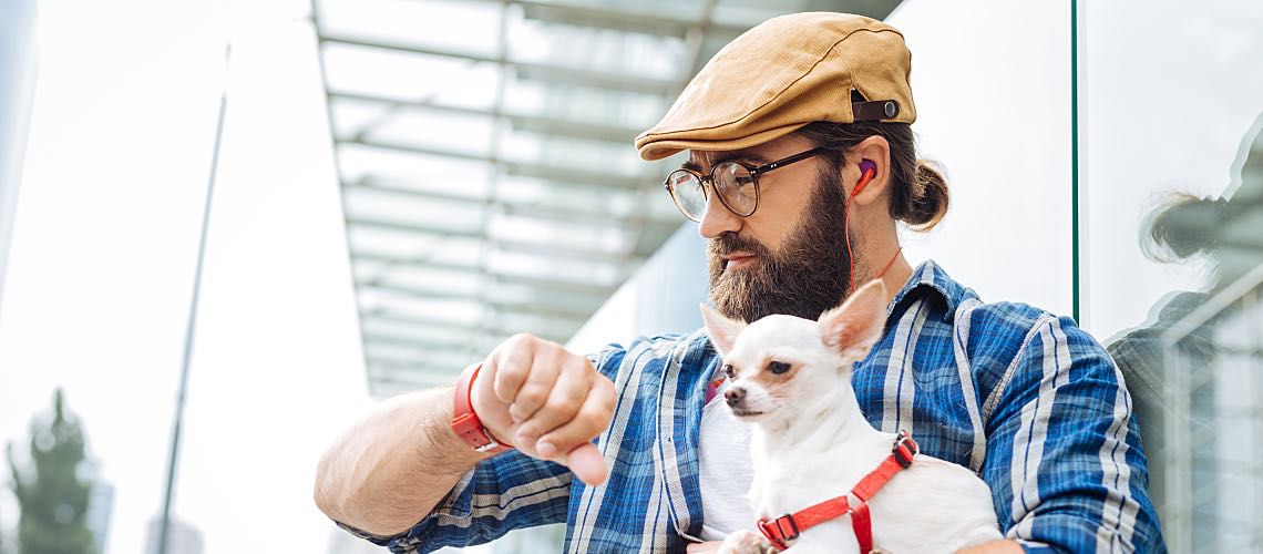 Man holding small dog looking at watch waiting for an appointment.