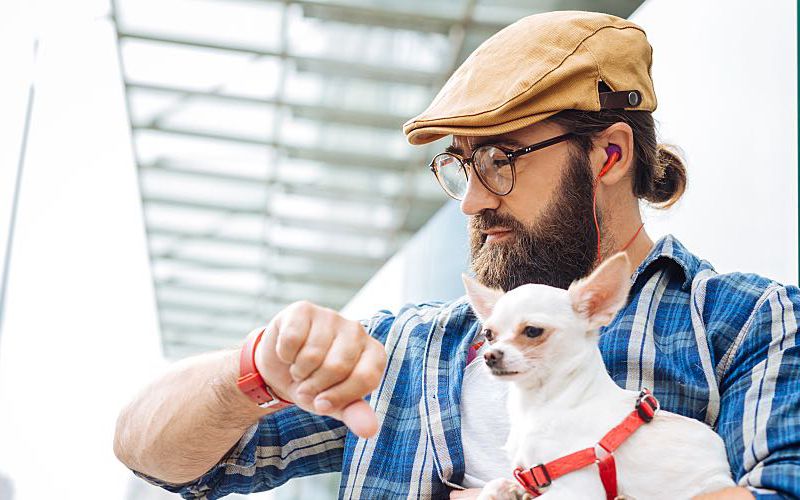 Man holding small dog looking at watch waiting for an appointment.