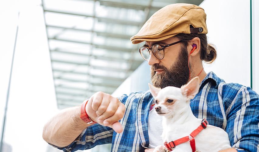 Man holding small dog looking at watch waiting for an appointment.