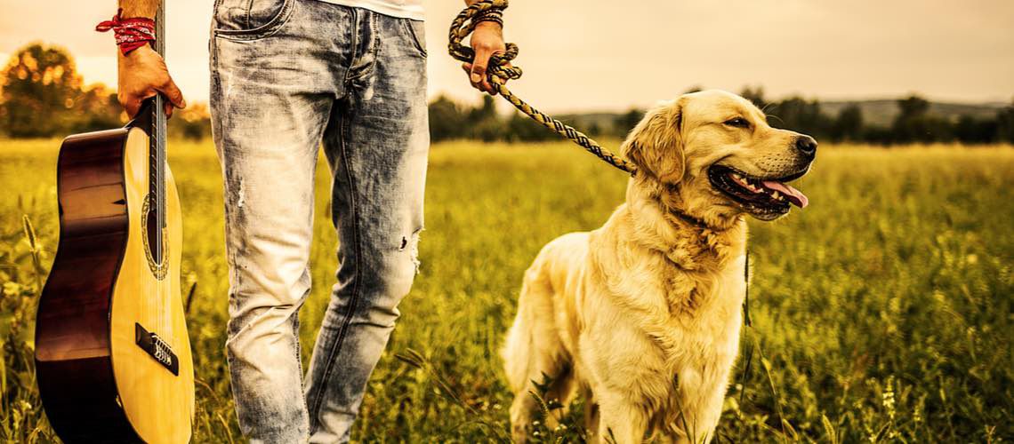 Man holding a guitar and walking a dog.