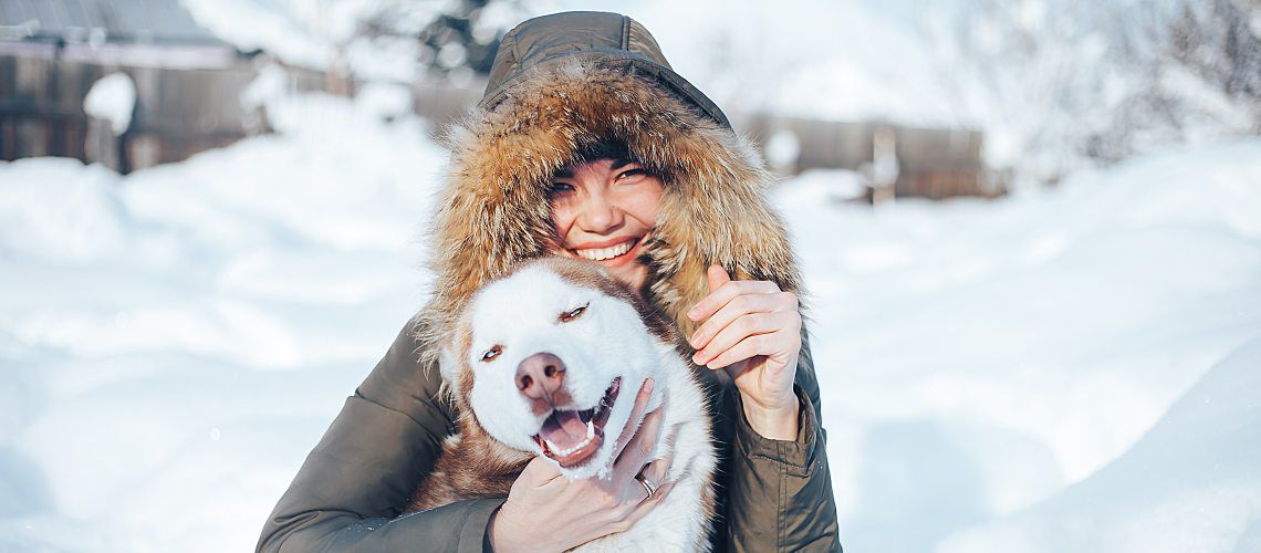 Young woman sitting in the snow with her dog.