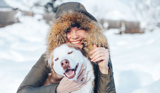 Young woman sitting in the snow with her dog.