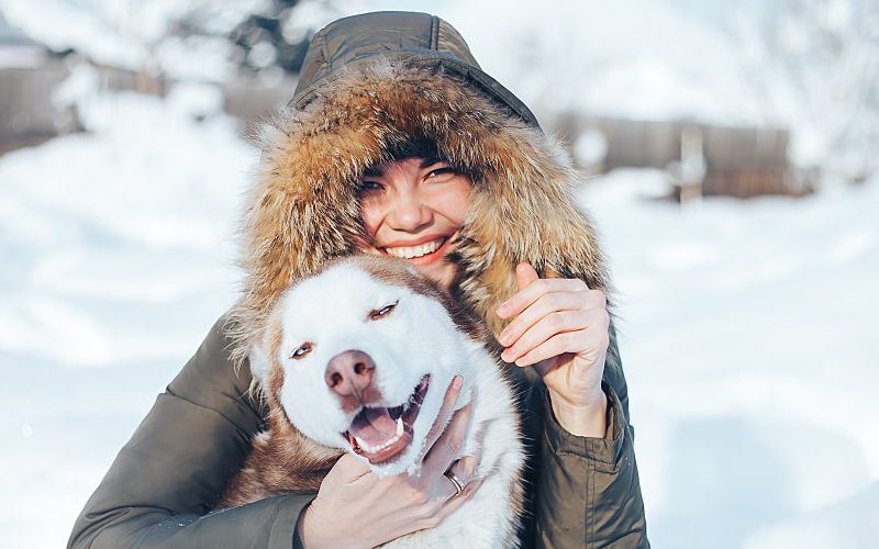 Young woman sitting in the snow with her dog.